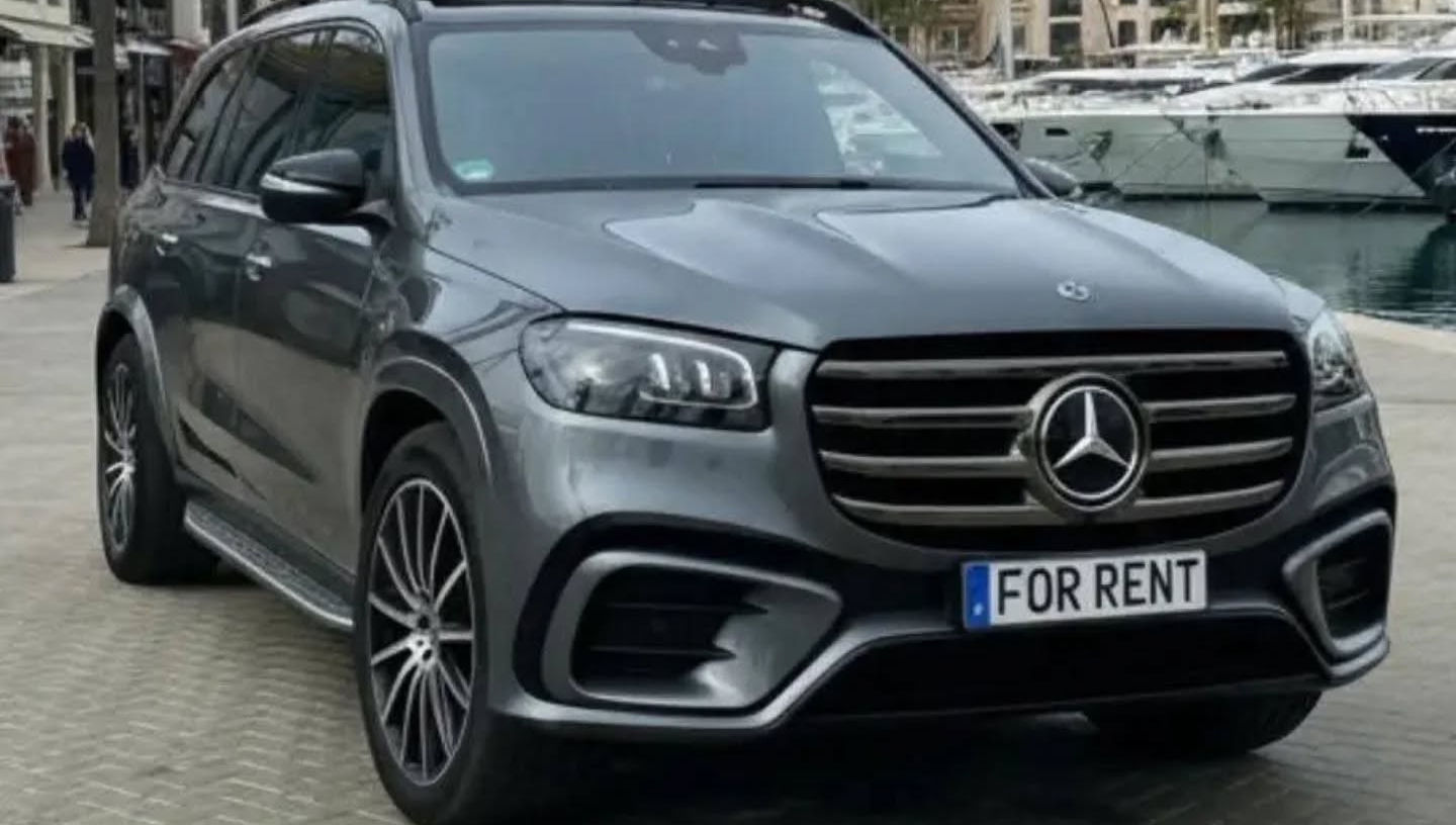 Front-right three-quarter hero shot of grey metallic Mercedes GLS 450d with bold grille, LED headlights and imposing SUV stance, premium family hire Marbella