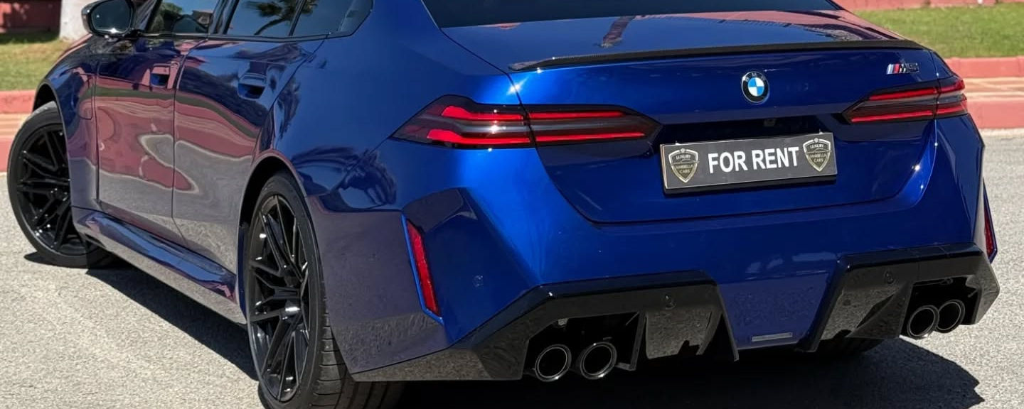 Majestic rear-left three-quarter hero angle featuring trapezoidal tailpipe layout, sculpted rear apron and extended wheelbase stance on BMW M5 Competition sedan, Marbella rental