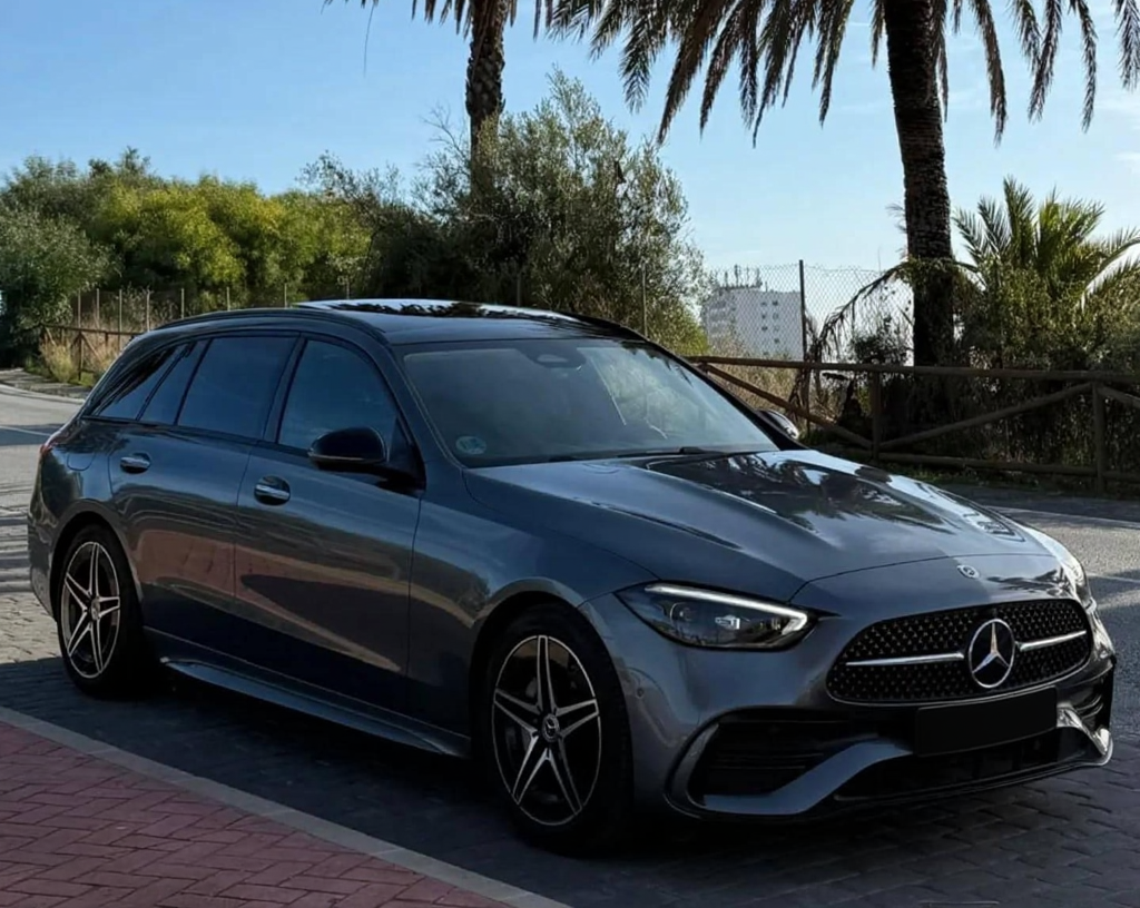 Front-right three-quarter hero shot of dark grey Mercedes C220d sedan with LED headlights, diamond grille and sporty front bumper, Marbella luxury car rental