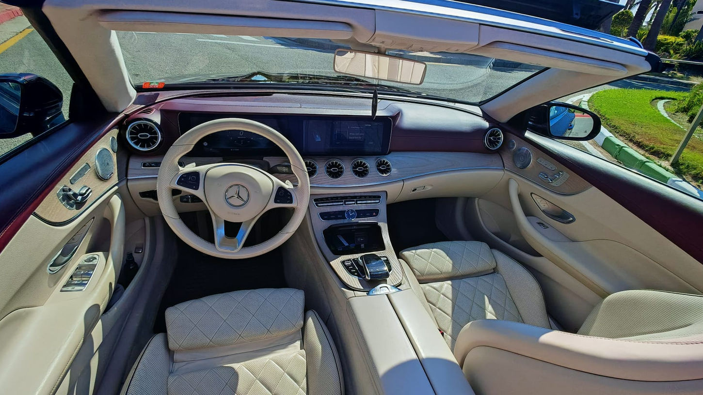 Driver-focused cockpit of Mercedes E450 Cabriolet featuring digital displays and luxury materials