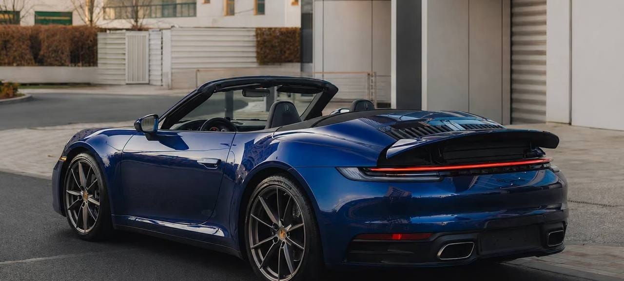 Blue Porsche 911 Carrera Cabriolet with the roof lowered, shown from the rear left.