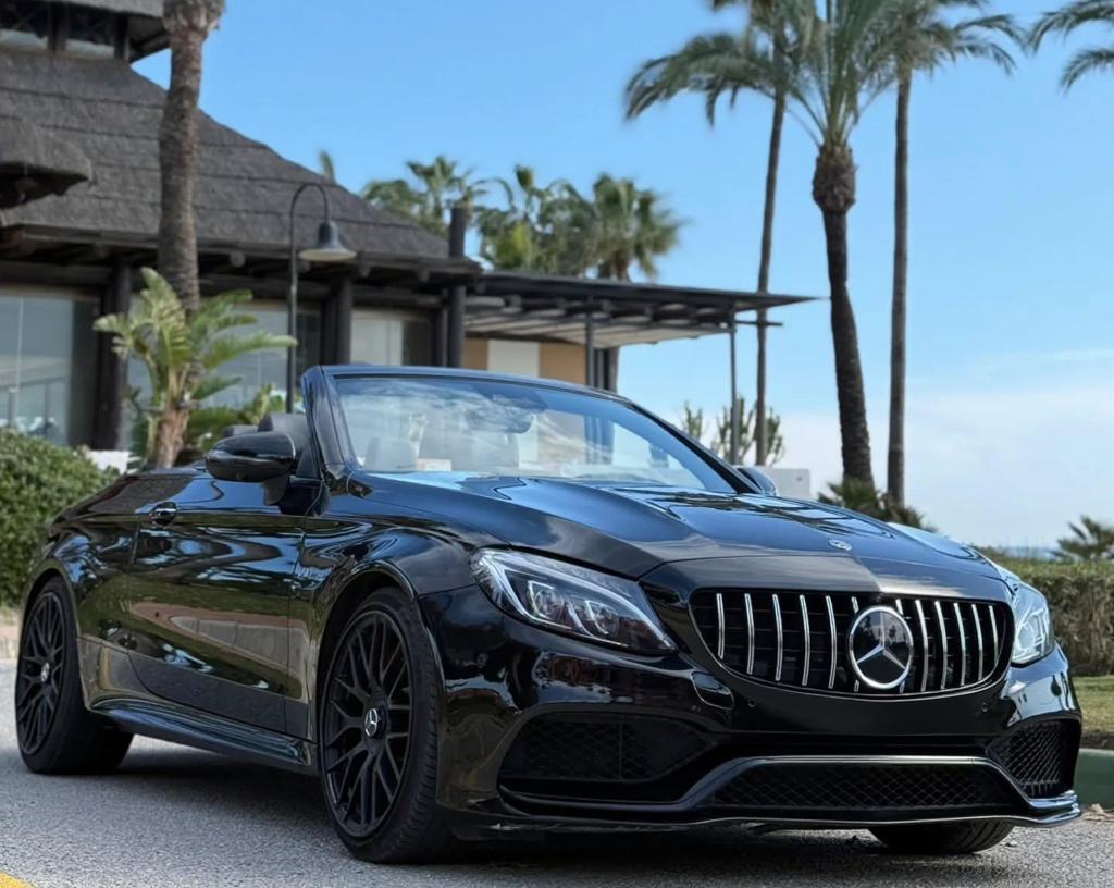 Front-right three-quarter hero shot of black Mercedes-AMG C63 S Cabriolet with AMG Panamericana grille, large air intakes and LED headlights, high-performance cabrio rental Marbella