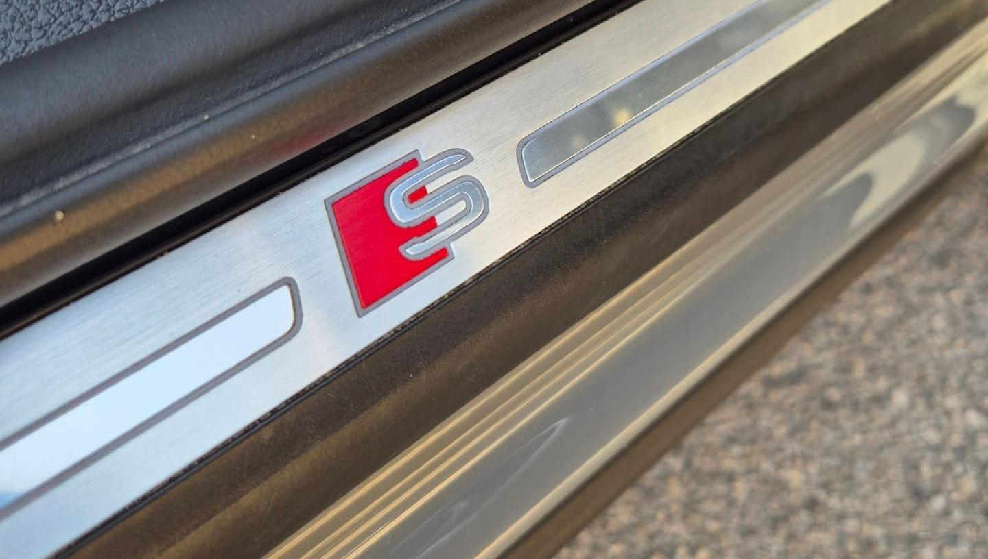Close‑up of illuminated S line logo on the interior door sill of Audi Q3 S‑line TDI, highlighting sporty trim detail.