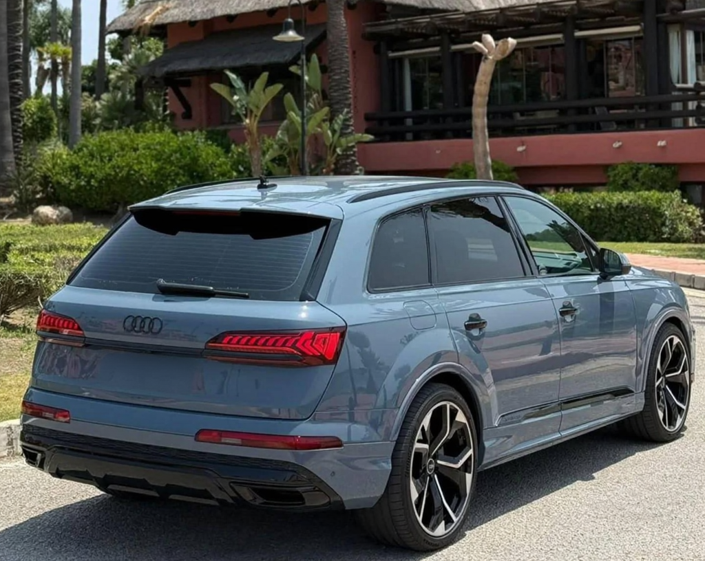 Rear right three-quarter hero view of Audi Q7 50 TFSI plug-in hybrid SUV with LED tail lights and roof spoiler, parked in Marbella.