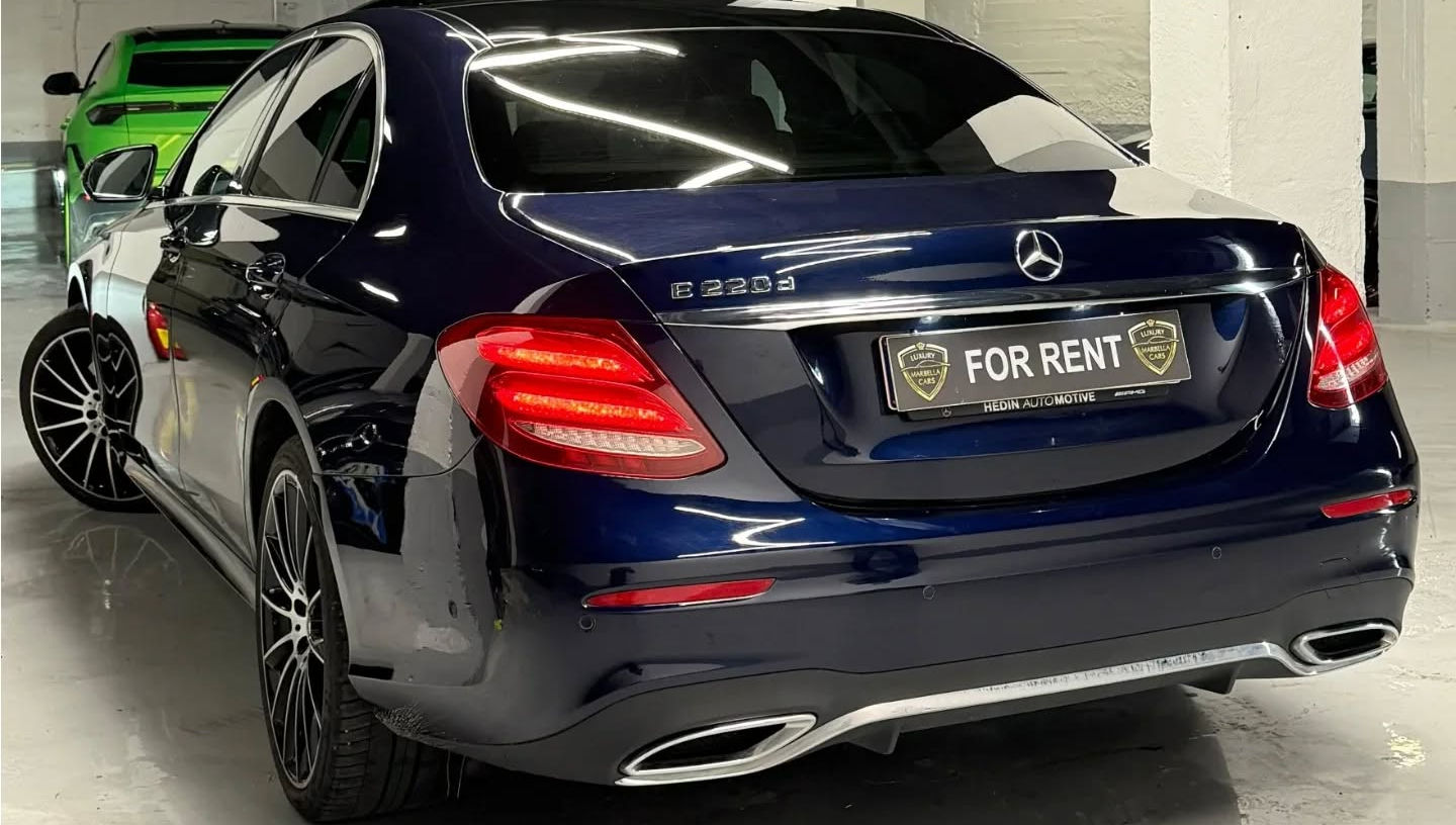 Rear-left three-quarter view of blue metallic Mercedes E220d highlighting sloping roofline, sculpted boot and stylish LED rear lights, Marbella executive car rental