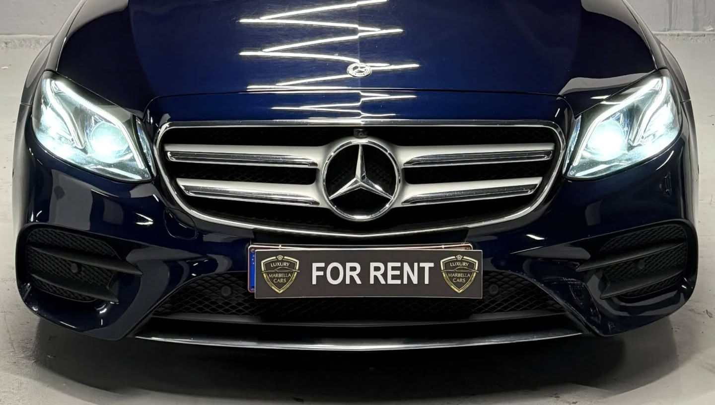 Head-on front view of blue metallic Mercedes E220d showing signature Mercedes grille, sharp headlamps and refined saloon design, Mercedes rental Marbella