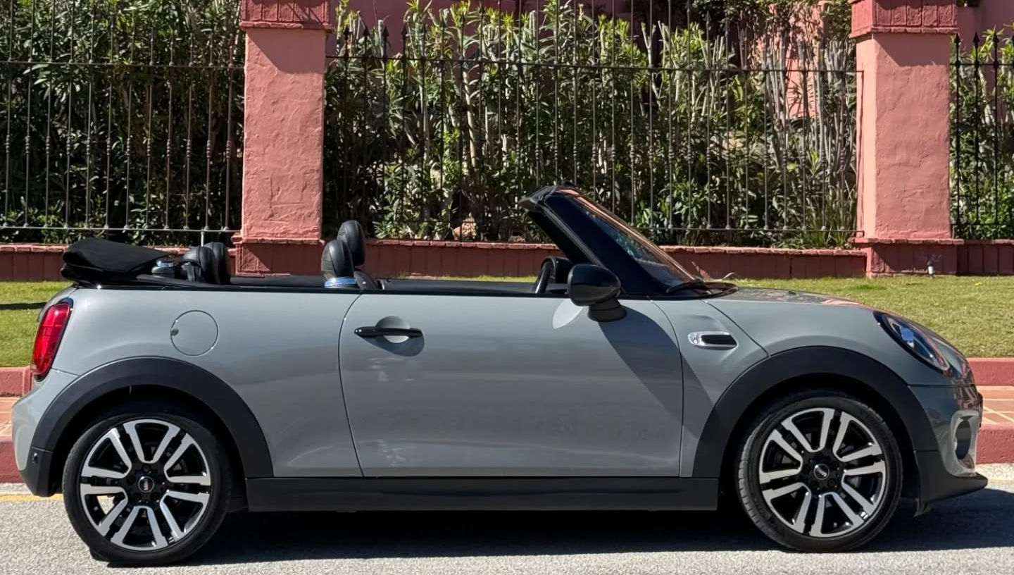 Right-side profile of grey metallic MINI Cooper Convertible with two-door body, lowered soft-top and alloy wheels, fun open-top car rental in Marbella