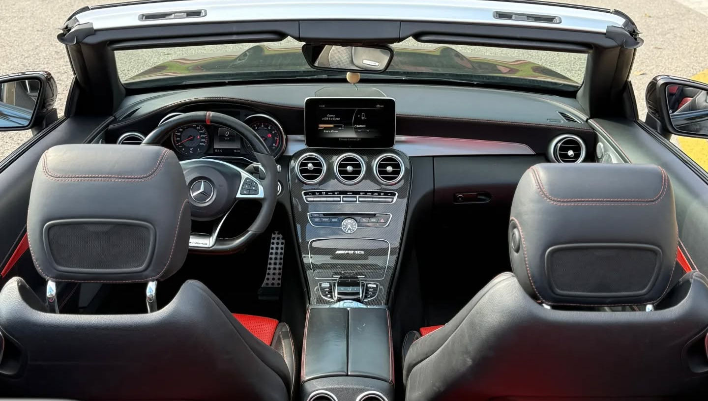 Wide interior view of Mercedes-AMG C63 S Cabriolet taken from rear seats showing both front seats, dashboard and center console with roof open, open-top AMG experience in Marbella