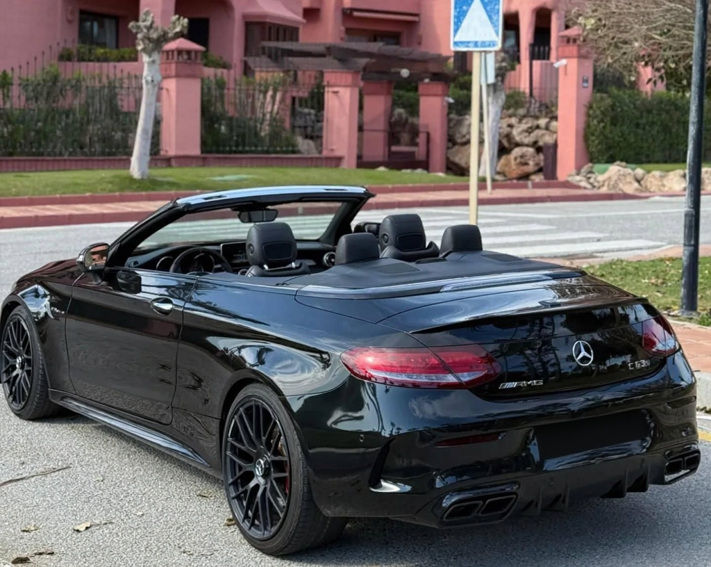 Rear-left three-quarter hero view of black Mercedes-AMG C63 S Cabriolet showcasing quad exhaust tips, diffuser-style rear bumper and slim LED taillights, AMG convertible hire Marbella