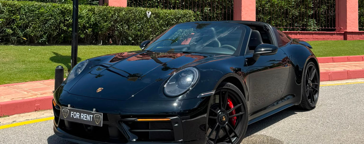 Black Porsche 911 Targa 4 GTS parked in Marbella with luxury beachfront residences in the background.