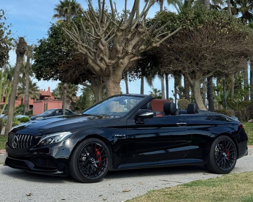 Left-side profile of black Mercedes-AMG C63 S Cabriolet with roof down, muscular rear haunches, multi-spoke AMG wheels and low, aggressive stance, Marbella luxury cabrio rental