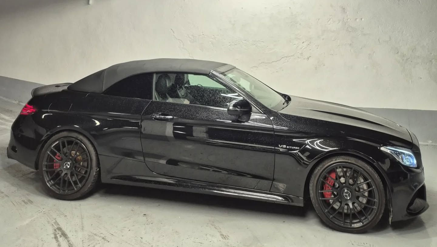 Right-side profile of black Mercedes C-Class cabriolet showing sleek two-door silhouette, fabric soft-top folded down and multi-spoke alloy wheels, Marbella convertible car hire