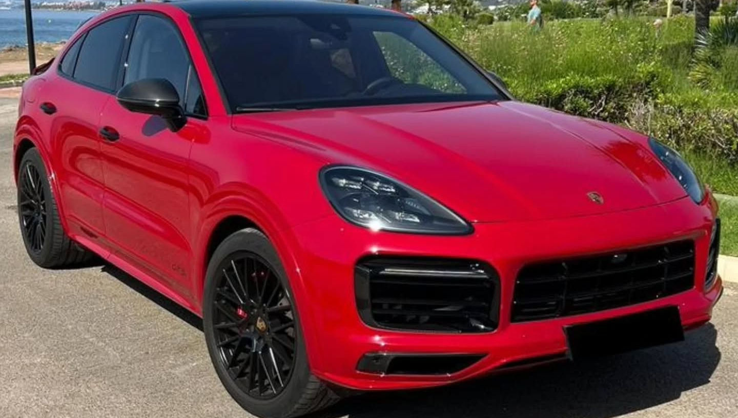 Front-right three-quarter hero shot of red Porsche Cayenne GTS highlighting sculpted bonnet lines, black trim details and large alloy wheels, luxury SUV rental Marbella