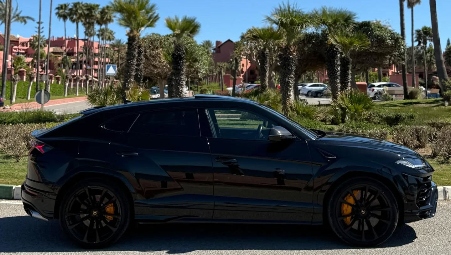 Right-side profile of black Lamborghini Urus emphasizing coupe-like roofline, strong character lines, large alloy wheels and powerful super SUV proportions, rent Lamborghini Urus Marbella