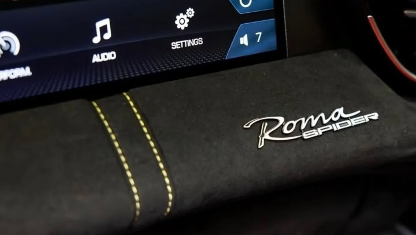 Close-up of Ferrari Roma Spider logo on the passenger side of the dashboard, highlighting model branding detail.