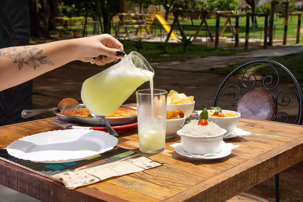 Mesa posta em restaurante mostrando pratos, ambiente e uma pessoa servindo um copo de limonada. Fotografia profissional para restaurantes