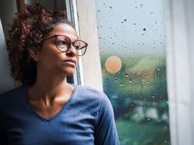 Une femme de race noire regarde par une fenêtre avec météo pluvieuse
