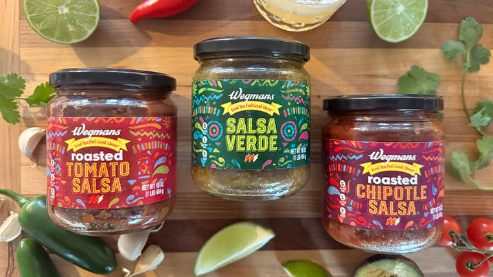 Three jars of Wegmans Roasted Salsa Verde, Tomato Salsa, and Chipotle Salsa on a marble counter with ingredients, and related foods surrounding them. Packaging recently designed by CINSYR in Syracuse, New York. 