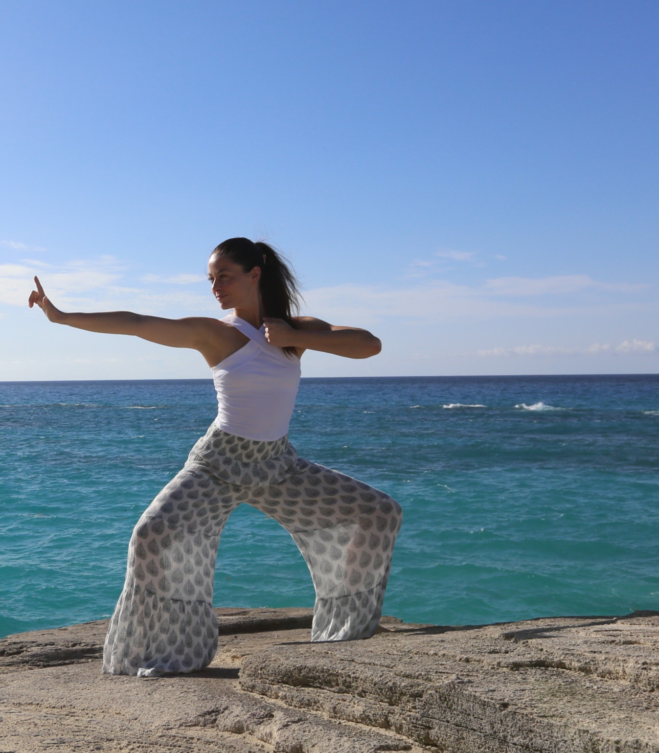 Reya Mithra standing on a beach with arms outstretched, ocean behind her