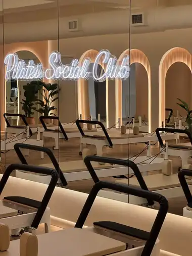 Reformer studio with the Pilates Social Club neon sign reflected in the mirrors