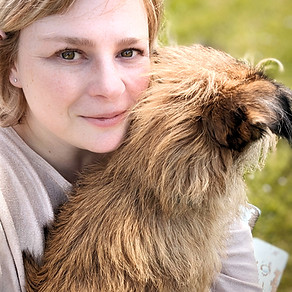 Gesicht von einer weiblichen Person und struppeliger hellrotbrauner Hund auf dem Schoß, man sieht den Kopf von hinten