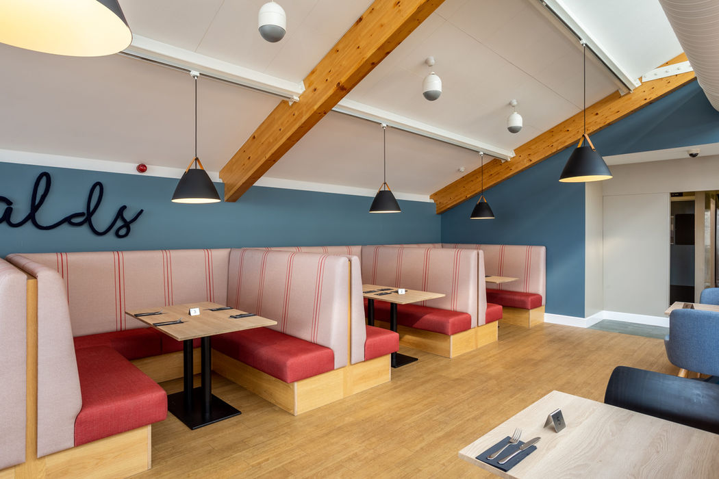 Booth/banquette red seating area with crocheted Oswalds signage on wall above and hanging pendant light at Cranstons Cafe Oswalds Penrith Foodhall