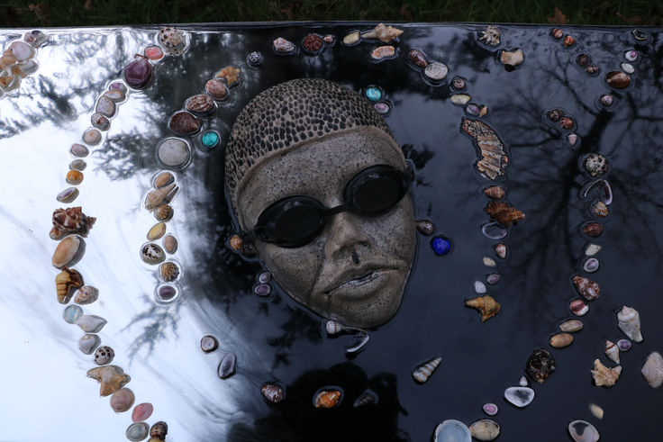 Installation artistique représentant une tête sculptée immergée dans une surface noire réfléchissante, entourée de coquillages. Œuvre contemporaine interrogeant la montée des eaux, la mémoire des océans et notre rapport à l'environnement. Art engagé, sculpture écologique, impact climatique