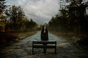 A senior high school girl wearing a short black dress and long black jacket, stands with a keyboard on a sand flats road.