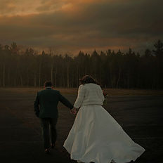 A bride and groom walk holding hands across a parking lot at sunset for their winter wedding