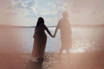 A couple's maternity session silhouette in Lake Placid NY with a lens flare against a cloudy blue sky just before sunset
