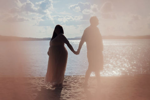 A couple's maternity session silhouette in Lake Placid NY with a lens flare against a cloudy blue sky just before sunset