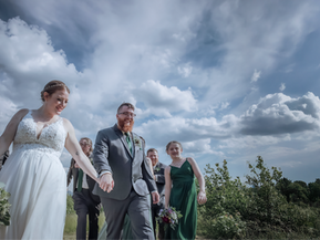 A bride and groom holding hands while walking in an Adirondack field with their bridal party behind them in early summer
