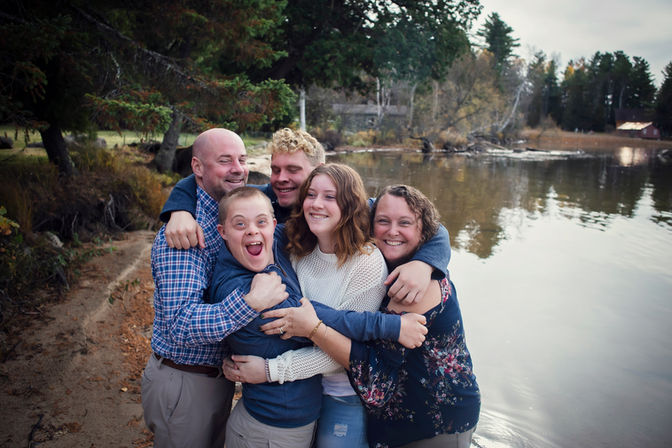 A family with a teenager hugging at the lake in the fall.