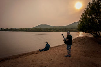 A father plays guitar to his autistic son while the sone wears a Micheals Myers mask and outfit sitting by Lake Placid in the Adirondacks