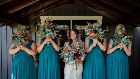 The bride and her bridesmaids posing with their bouquets in front of a rustic cabin.