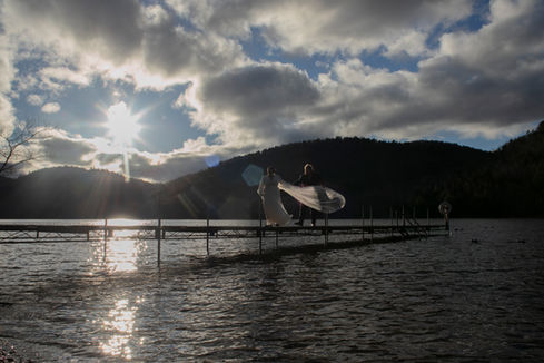 An Adirondack Coast wedding photo of a bride and groom walking on a dock on Lake Champlain with her veil in the wind in late fall.
