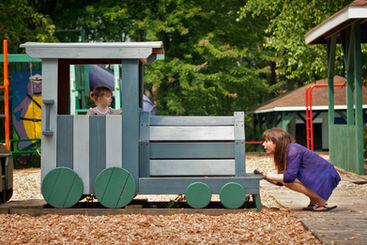 A mom and her child at a playground with a large wooden train.