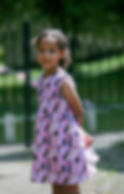 Little girl from 1st image in same Barbie dress, arms behind back smiling off camera.