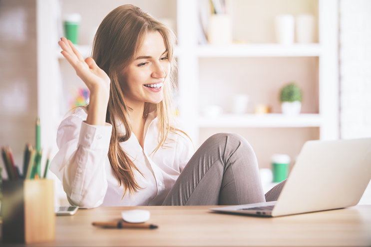 A smiling woman waves at her laptop while siting at a table. This could represent the peace of mind of knowing their private practice paperwork is approved and legally sound. Contact us to learn of our free HIPAA form and other free forms needed for counseling in a private practice