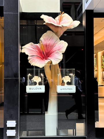 Window display with a large pink flowers and small bright flowers in the display cases