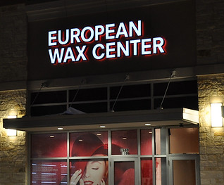 European Wax Center light up channel letter wall sign; and lady in red hat perforated window graphic applied to storefront glass