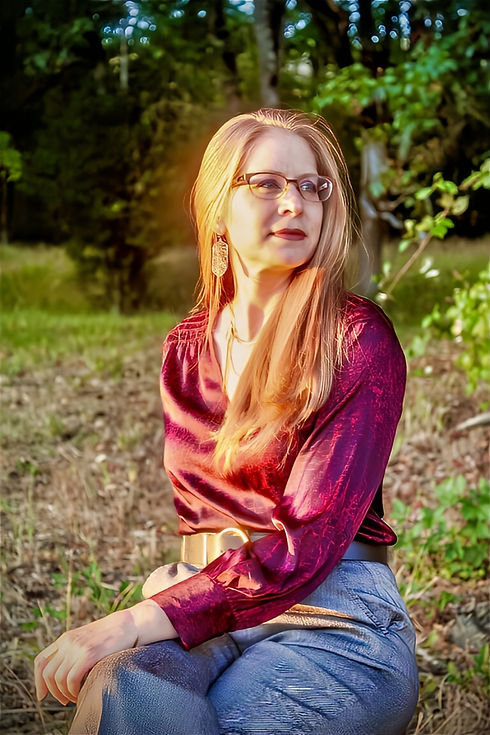 Gretchen sits on the grass, wears glasses, and has long blond hair.