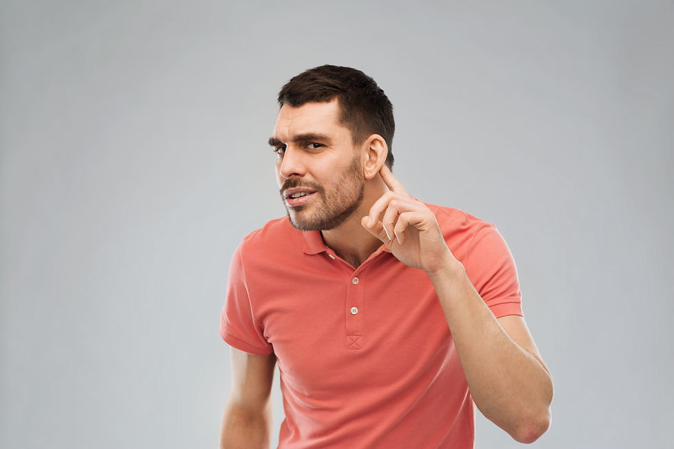 A confused looking man holds his index finger behind his ear.