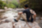 A man with a backpack sits by a river