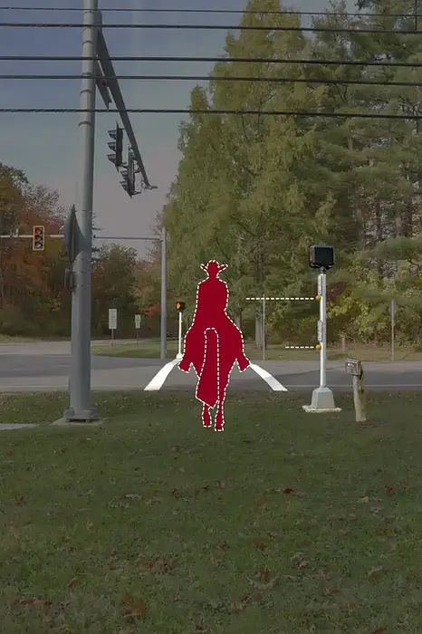 Pedestrian crosswalk at a 4 way intersection. There is an image of a man on horseback to show that the traffic signal is at a height that will allow it to sense people traveling on horseback. There are trees in the background and a grassy area.