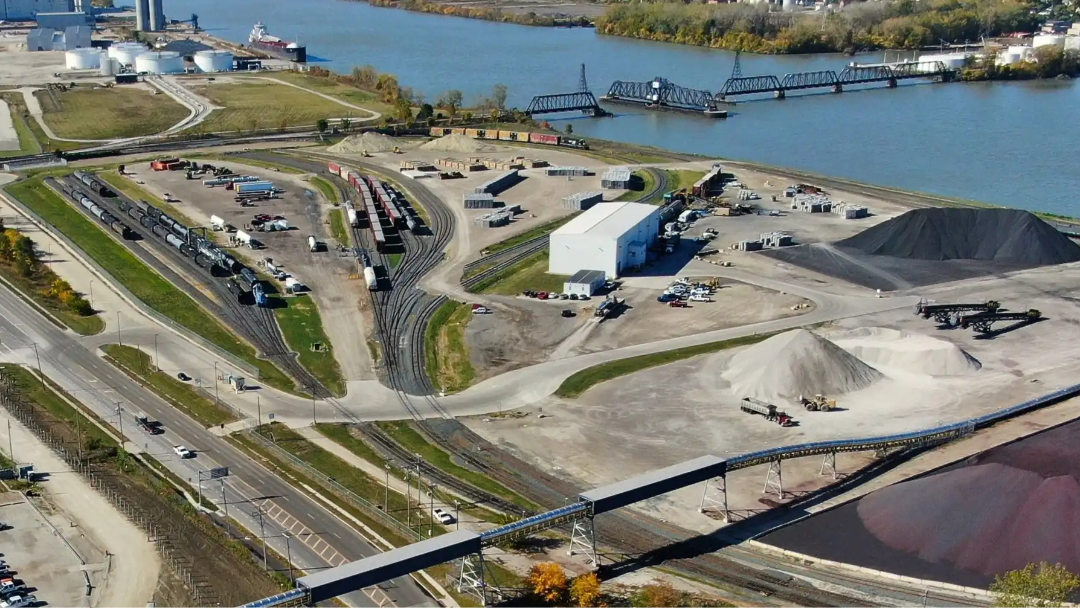 Aerial photo of industrial port including many rail spikes with occupying train cars. Large iron ore piles lay along the Maumee River