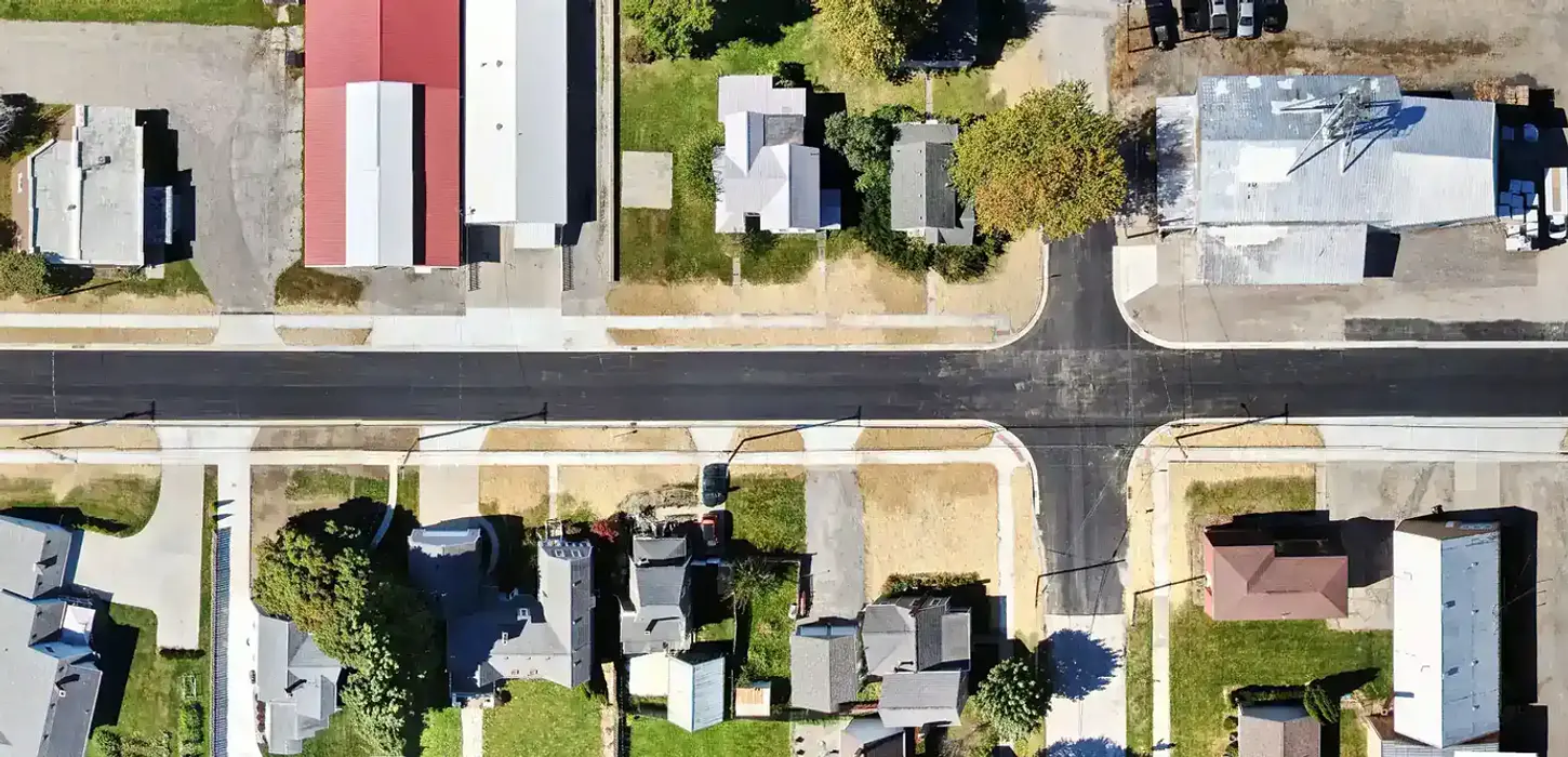 Aerial top-down panoramic photo of a newly paved asphalt roadway, new concrete sidewalks, and surrounding buildings.