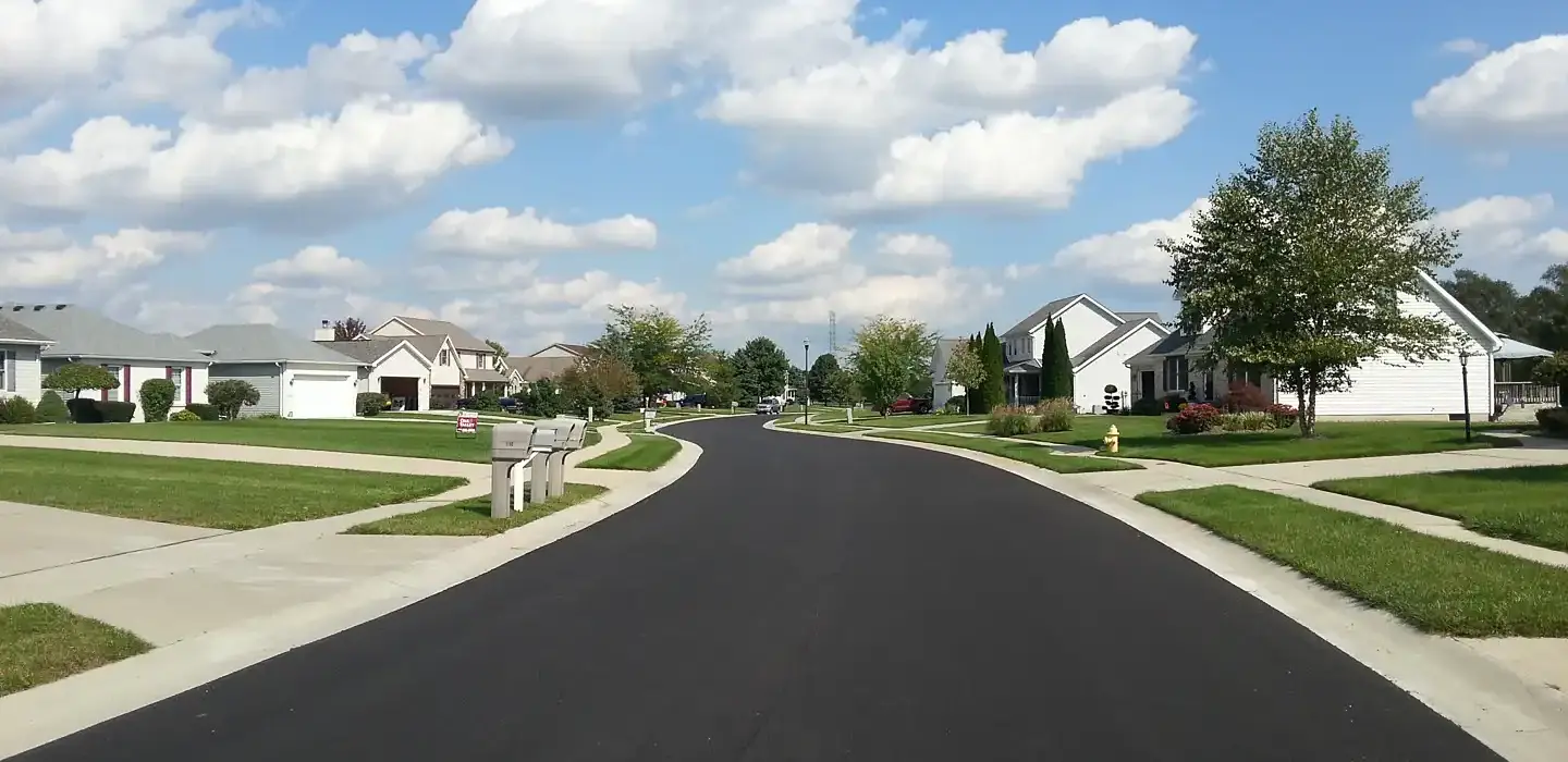 Fresh asphalt has been applied to a road that runs through a subdivision. There are houses on each side of the road.