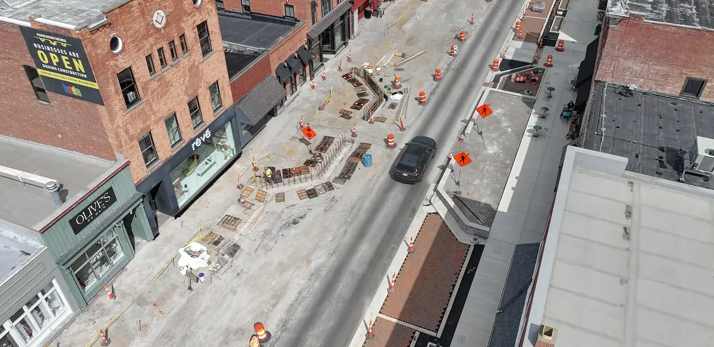 Downtown streetscape construction site with car passing through. Both Road and Walkway are under construction. Focus on pedestrian crossing bump-outs