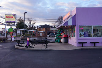 Kline's Dairy Bar with some Christmas inflatables outside and a Christmas-themed ice cream cone sign attached to the regular sign. The scene is angled so that you see the pastel purple Kline's building from the side and are facing the sign and picnic tables in front of the restaurant.